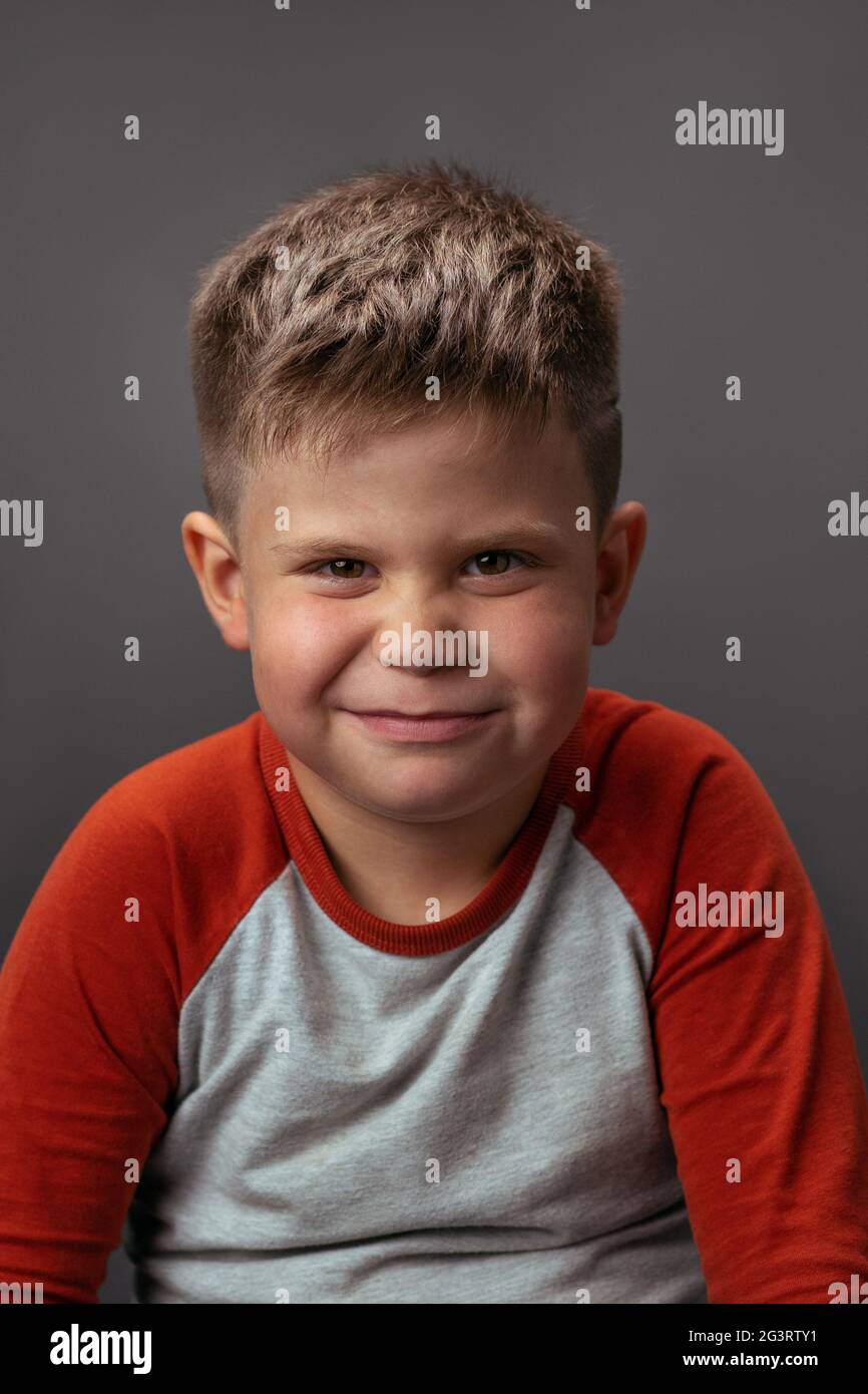 Preschool boy smiling with smirk at camera. Portrait of funny child on gray background. Emotions concept Stock Photo