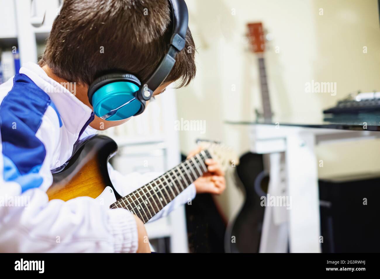 boy playing the electric guitar with blue headphones in a recording studio, horizontal Stock Photo