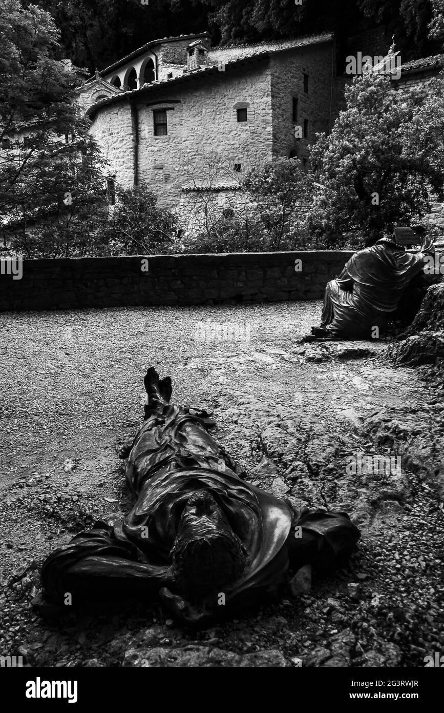 Assisi, Umbria, Italy: the statue of St. Francis lying on the ground while observing the stars in the night in front of the hermitage of prison Stock Photo