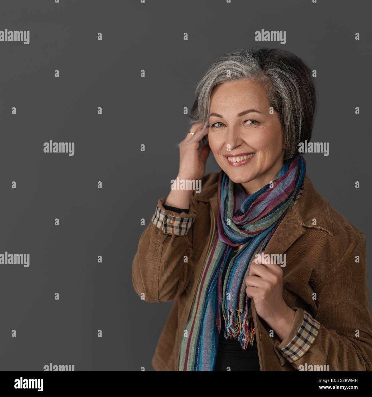 Creative mature woman in casual touching her graying short hair. Studio portrait on gray background. Copy space at left Stock Photo
