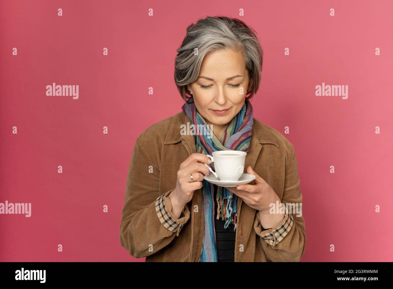 Charming elegant woman drinks coffee or tea holding white cup looking on it. Isolated on pink background with copy space. Studio Stock Photo