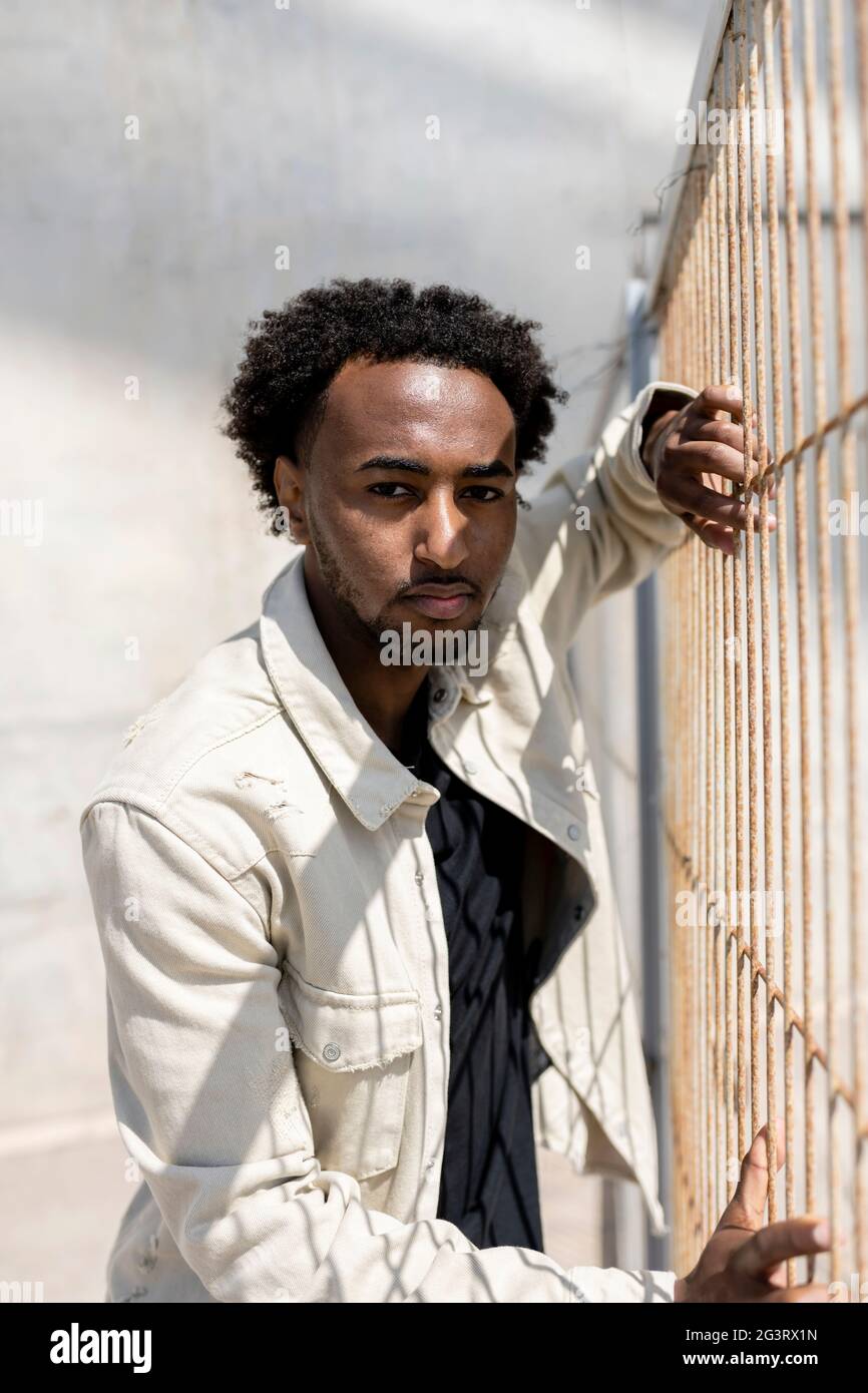 Afro man leaning on metallic fence while looking at camera Stock Photo
