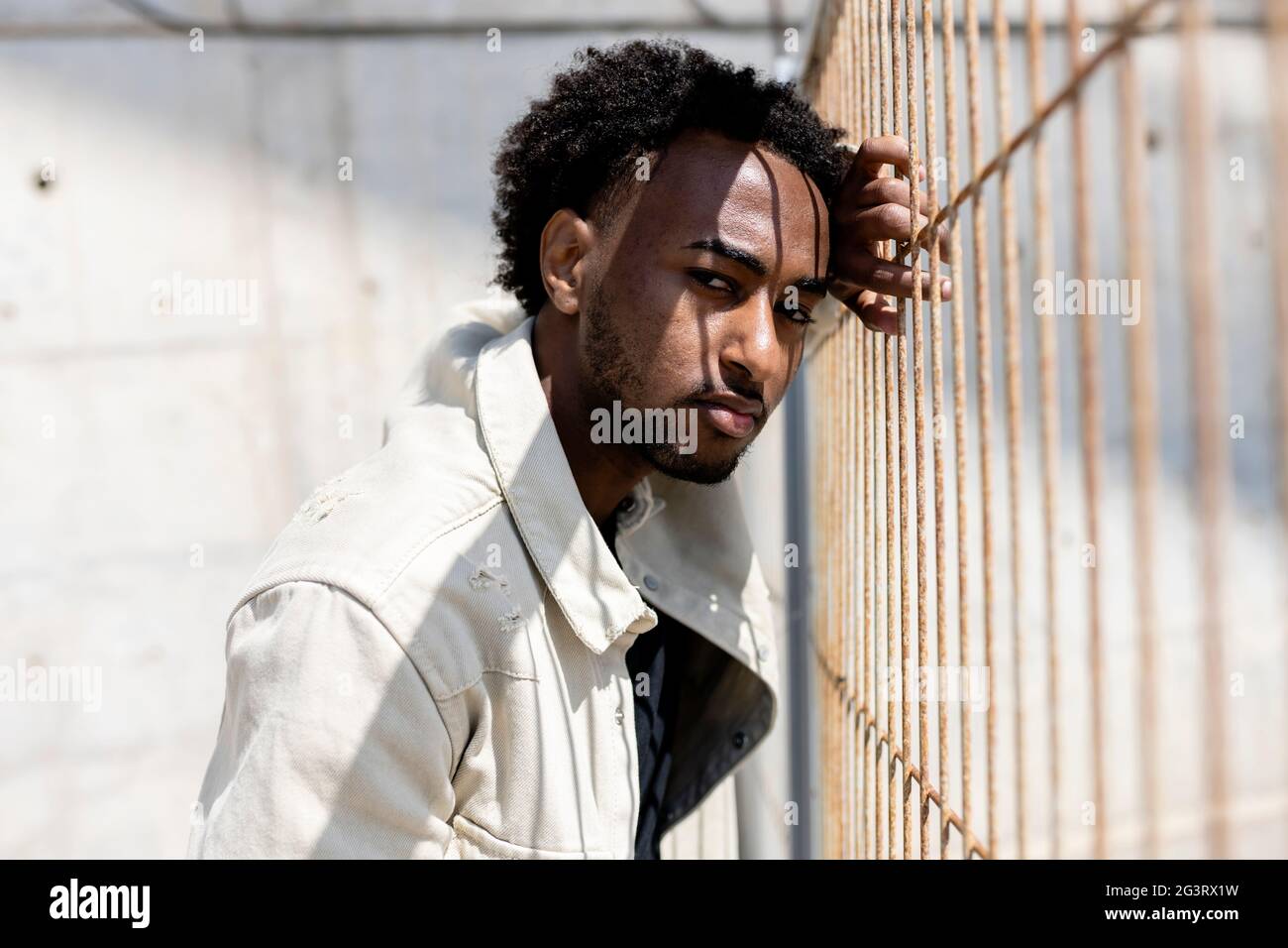 Afro man leaning on metallic fence while looking at camera Stock Photo