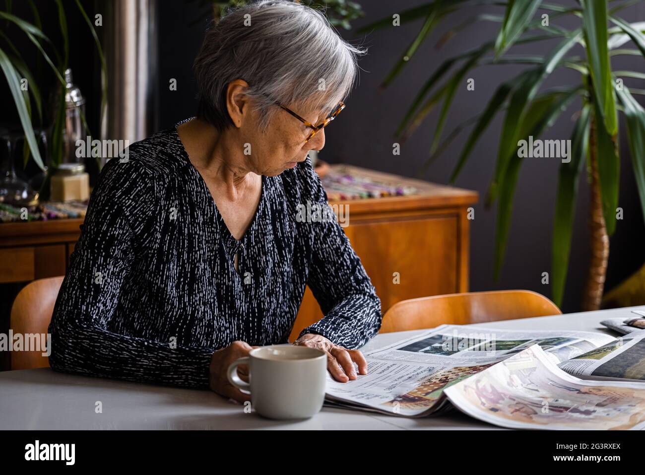 Senior woman reading newspaper while sitting at table with coffee Stock Photo