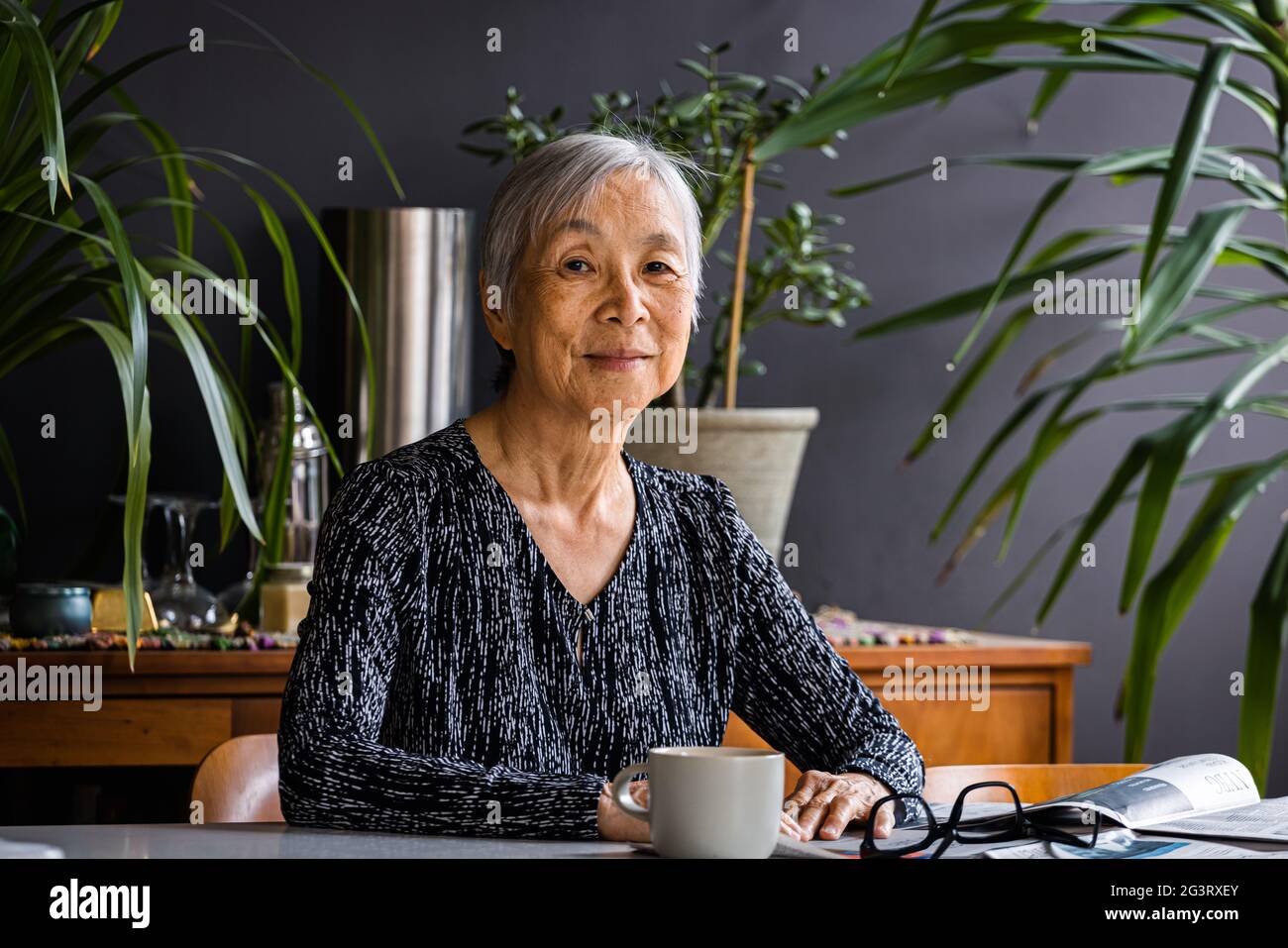 Portrait of smiling asian Senior Woman sitting at table at home Stock Photo
