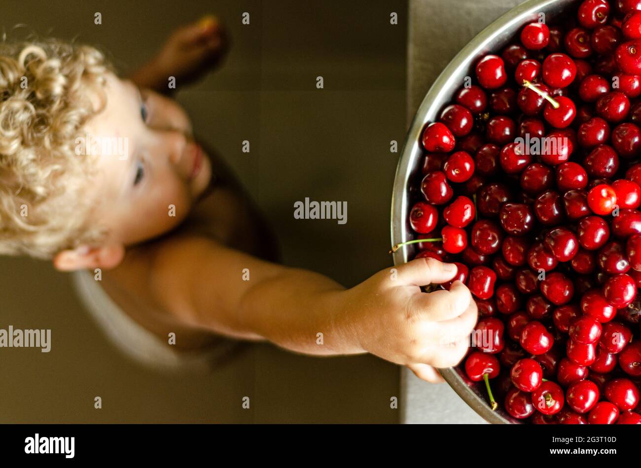 boy 2 years old reaching for a cherry, top view Stock Photo