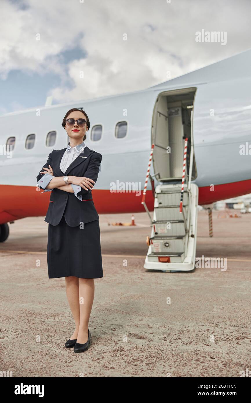 Confident stewardess on runway near airplane jet Stock Photo