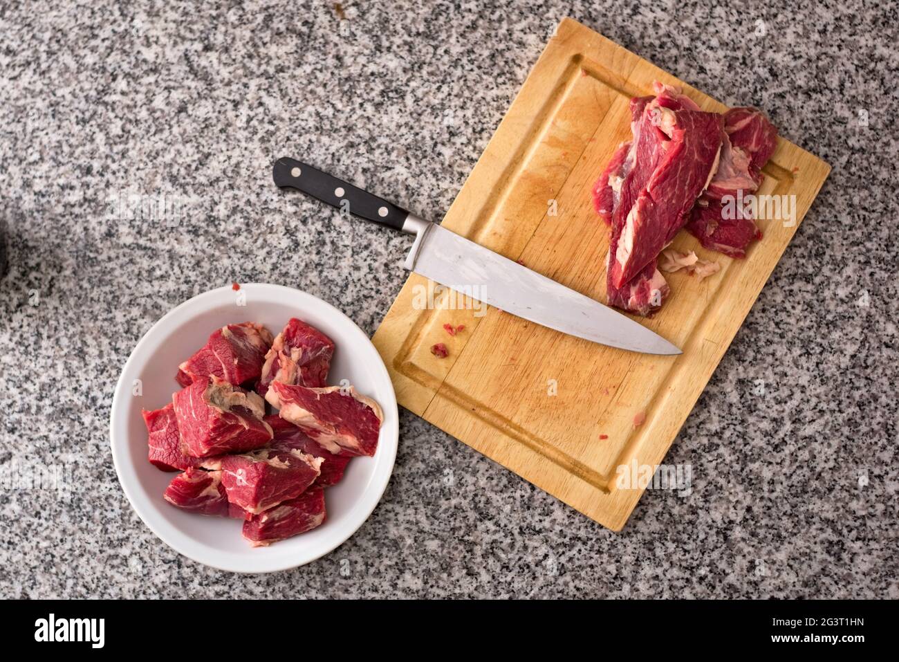 Diced, fresh red meat on a deep dish and kitchen knife over a wooden cutting board. Top-down view. Stock Photo