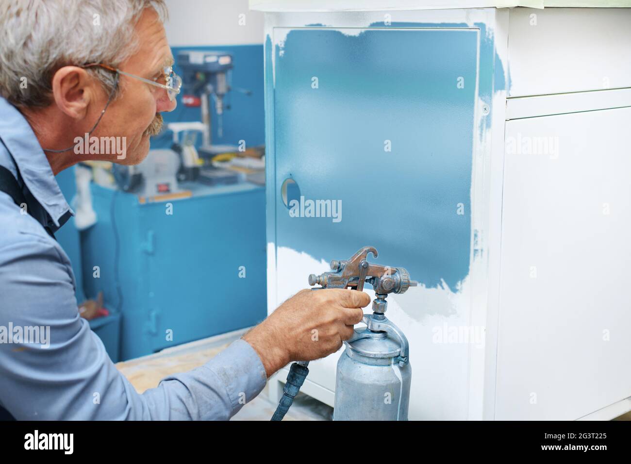 Painting of metal products. An elderly man paints a Cabinet with a compressor Stock Photo