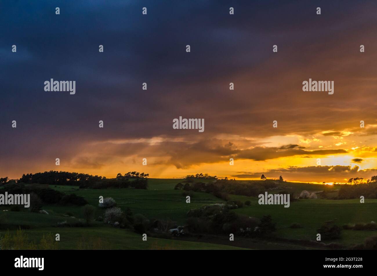 Dramatic cloudy sky at sunset over hilly grass covered landscape in Eifel, Germany Stock Photo