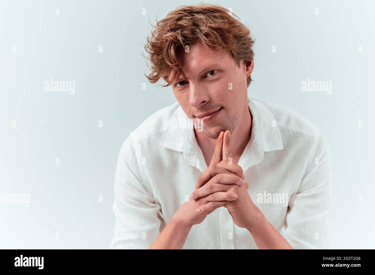 Young attractive man folded hands. Caucasian red haired guy in white shirt isolated on white background with copy space at left. Stock Photo