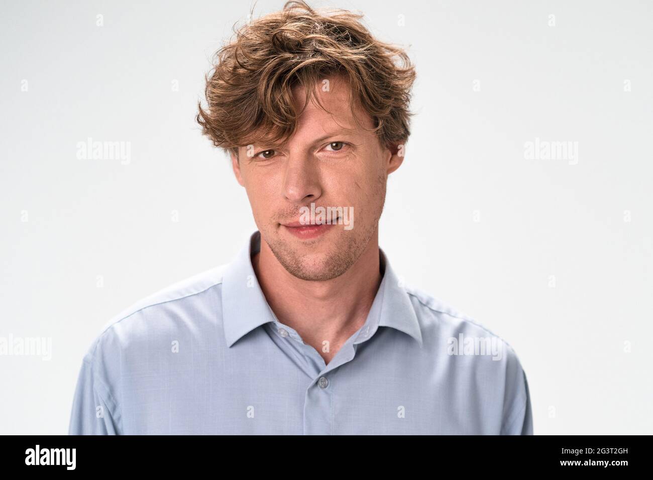 Slightly smiling man isolated on white background. Hazel eyes Caucasian  macho with curly red hair wearing light blue shirt looks Stock Photo - Alamy