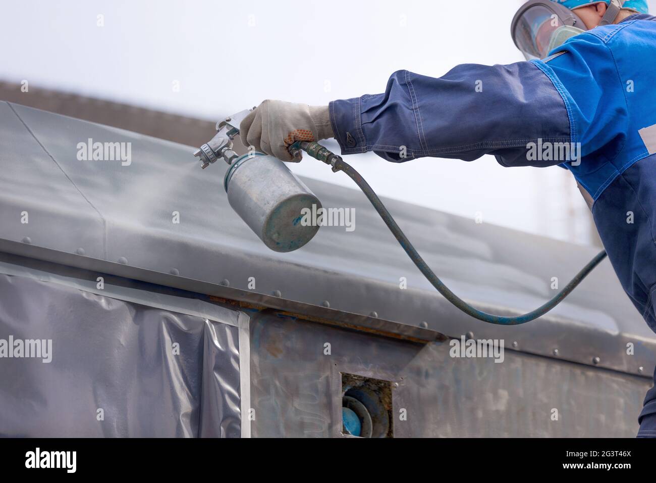 Industrial work. Priming of metal products from the compressor gun. A worker in overalls and a protective mask paints the body o Stock Photo