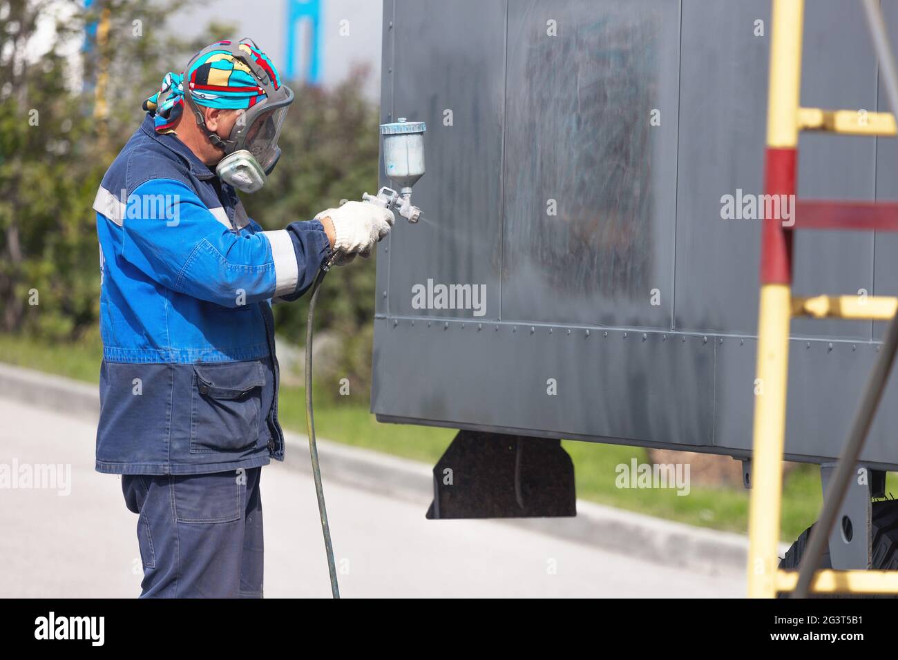 Industrial work. Priming of metal products from the compressor gun. A worker in overalls and a protective mask paints the body o Stock Photo