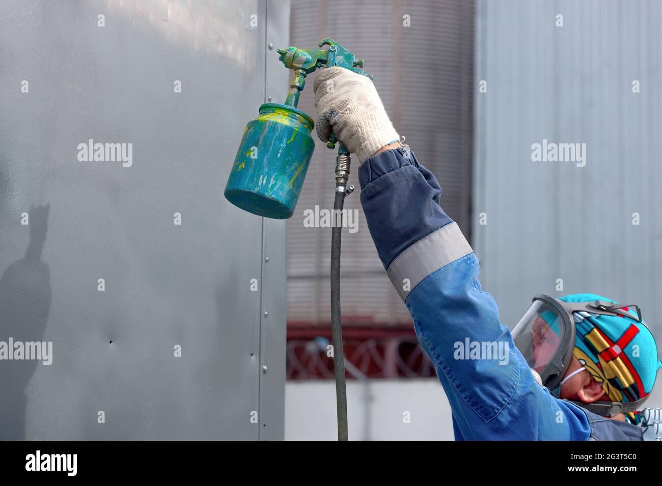 Industrial work. Priming of metal products from the compressor gun. A worker in overalls and a respi Stock Photo