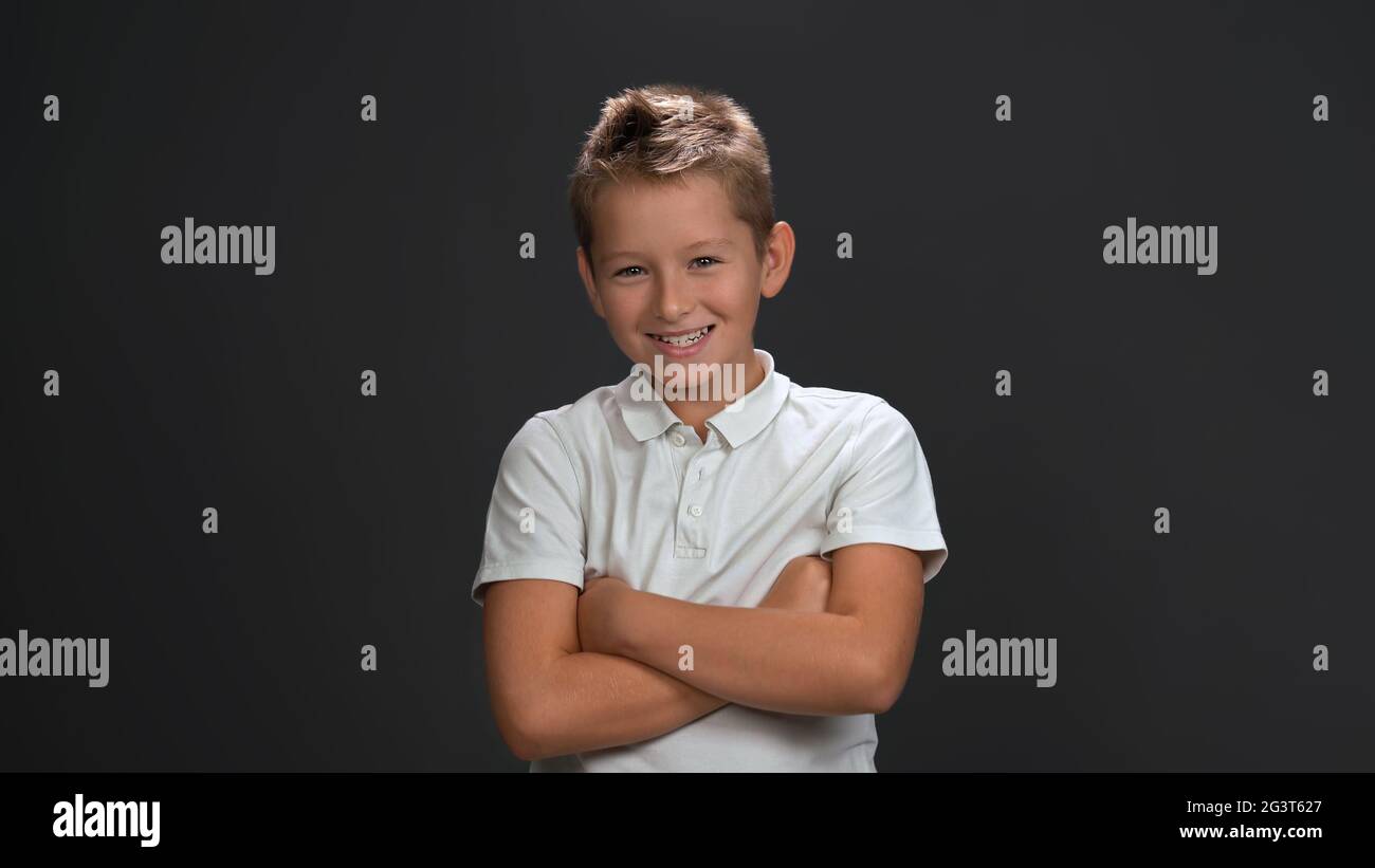 Happy teenager 10-12 years old boy broadly smiles crossed hands. Emotions concept. Isolated on gray background. Copy space Stock Photo