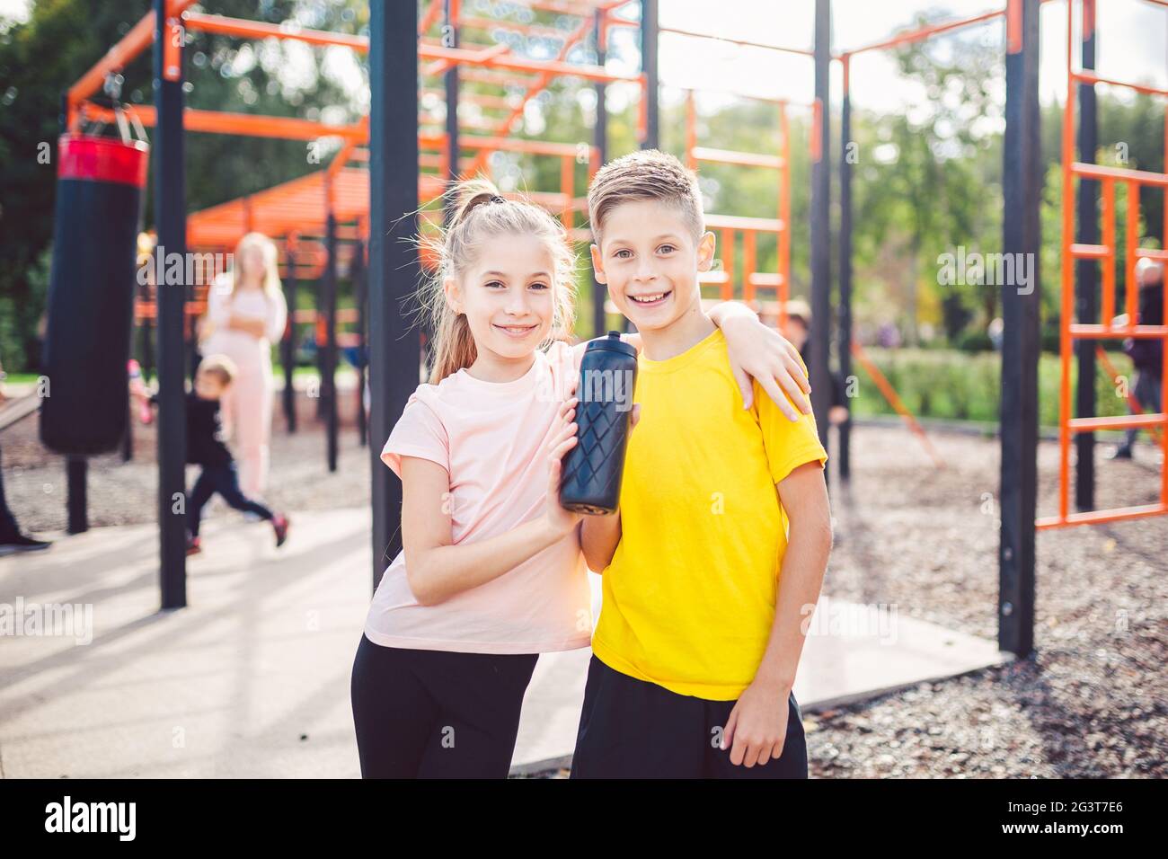 Sportive friends. Brother and sister standing together at street city gym. Children athletes hug smile during workout training. Stock Photo