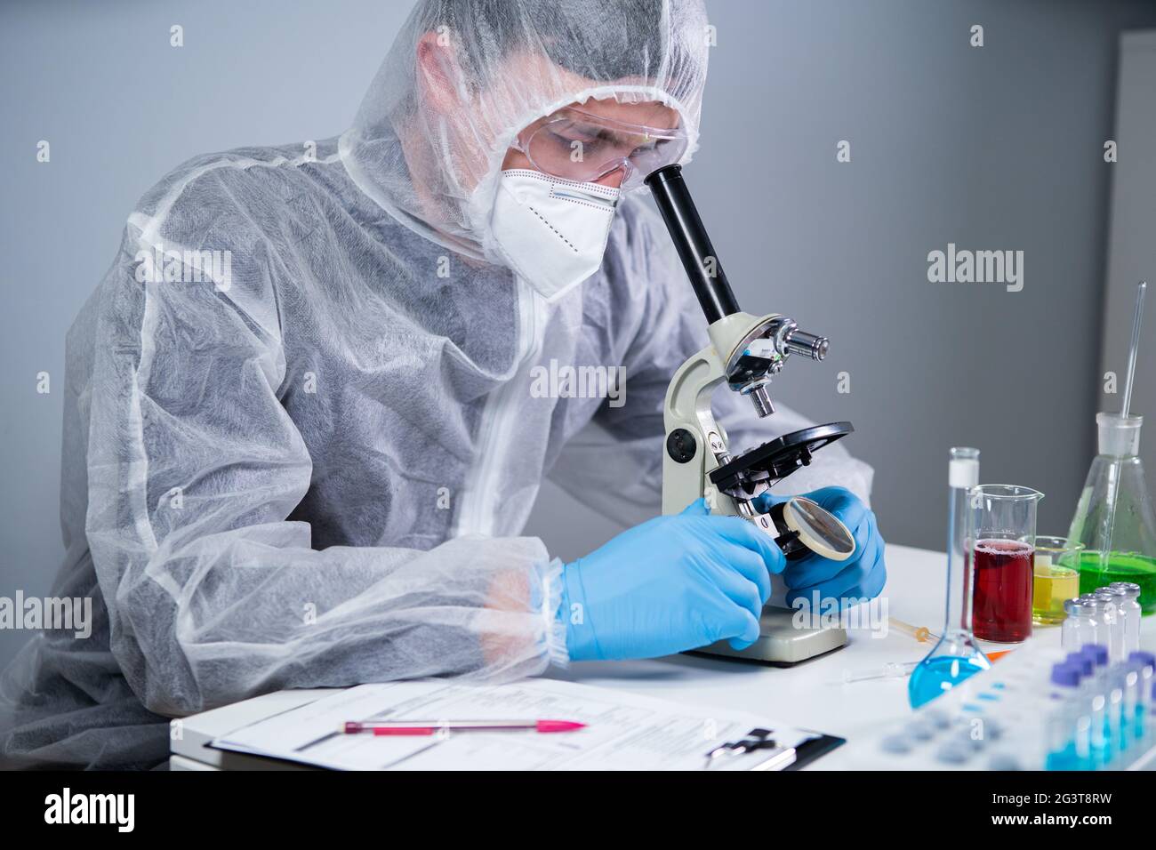 Scientist examining sample with a microscope, doing medical research in science laboratory. Male laboratory assistant in protect Stock Photo