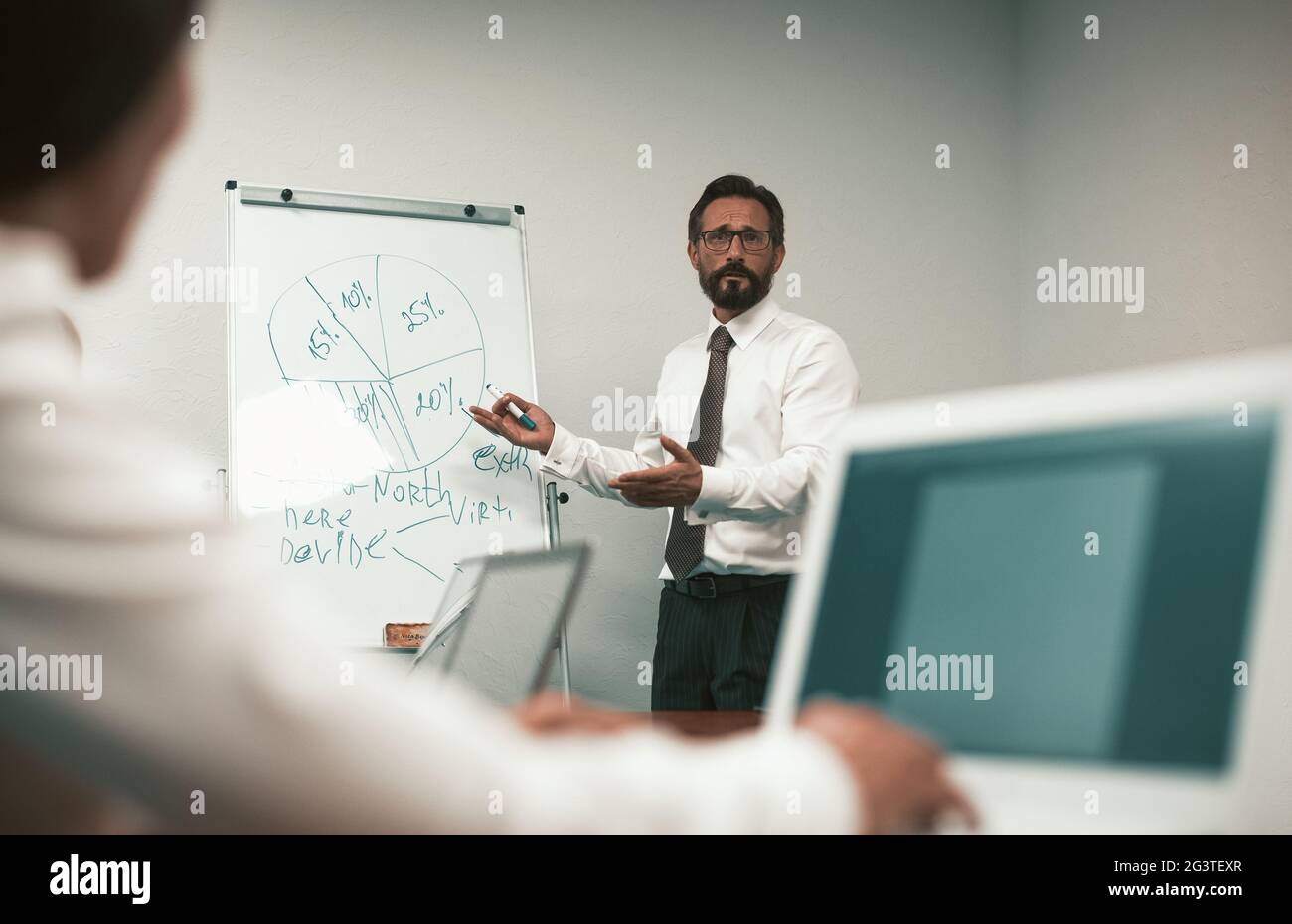 Mature man making business presentation or conference. Speaker man stands near whiteboard having discussion with business people Stock Photo