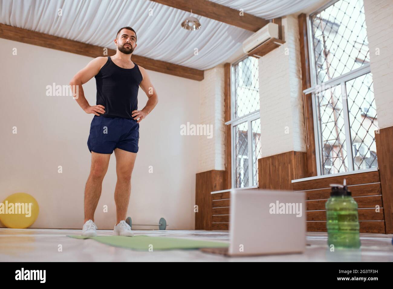 Athlete man trains hard in empty gym or home standing infront of laptop. Self isolated and motivated young man warm-up doing spe Stock Photo