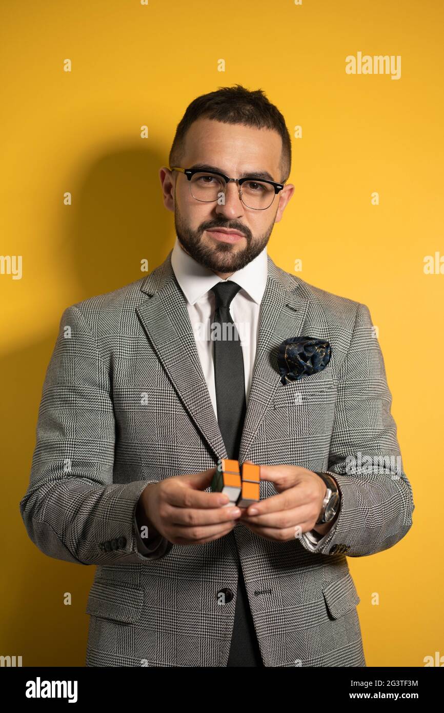 Smart young bearded handsome man in eye glasses wearing a suite holds a solved Pocket Cube 2x2x2 rotatable puzzle in hands while Stock Photo