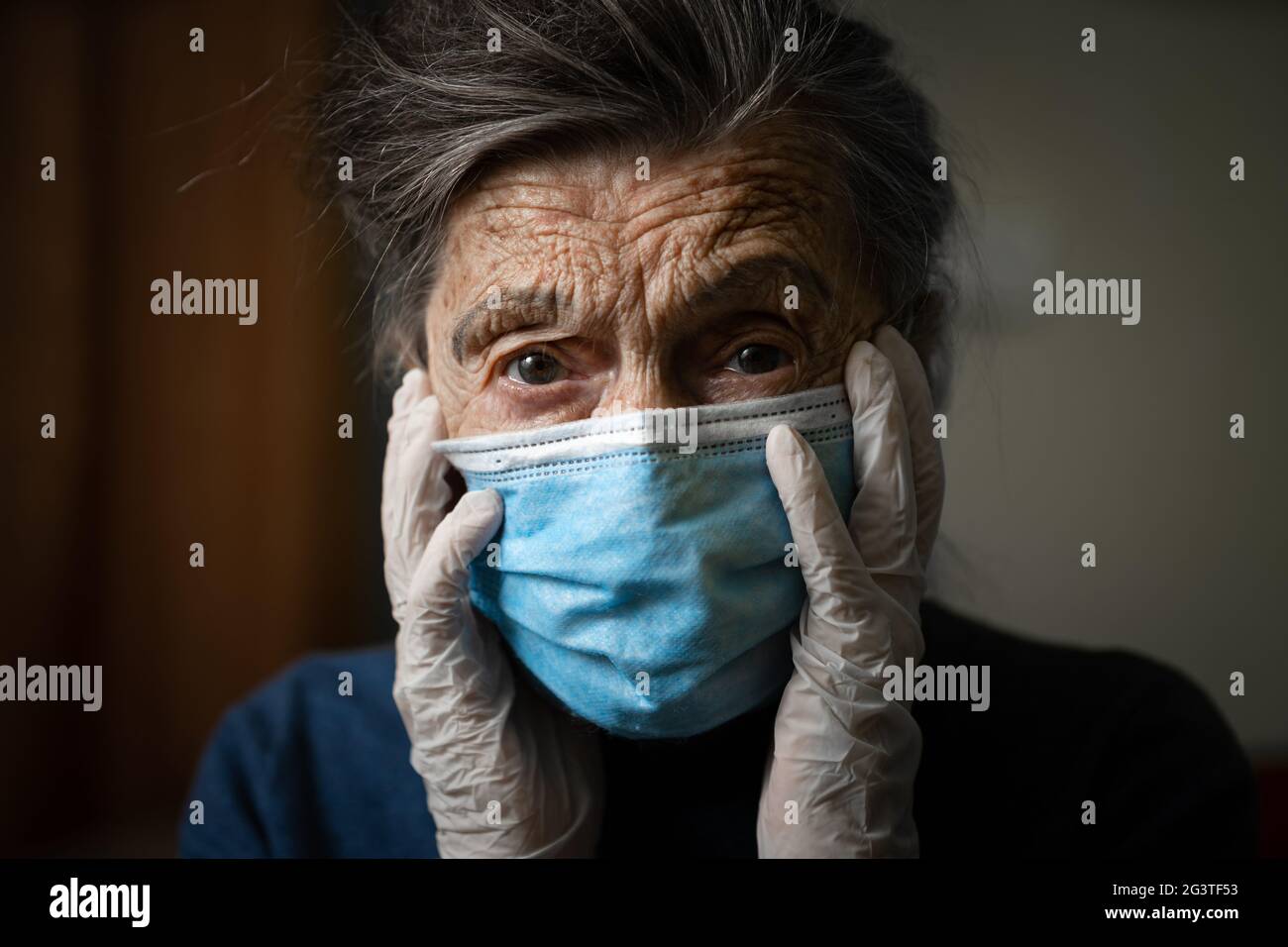 Portrait of an elderly Caucasian woman with wrinkles, wearing a medical mask and gloves, the emotion of fright and unpredictabil Stock Photo