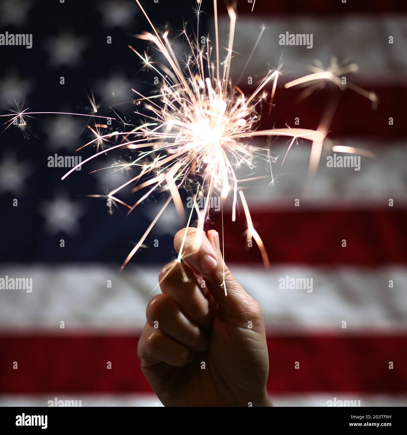 Hand holding lit sparkler in front of the American Flag for 4th of July ...