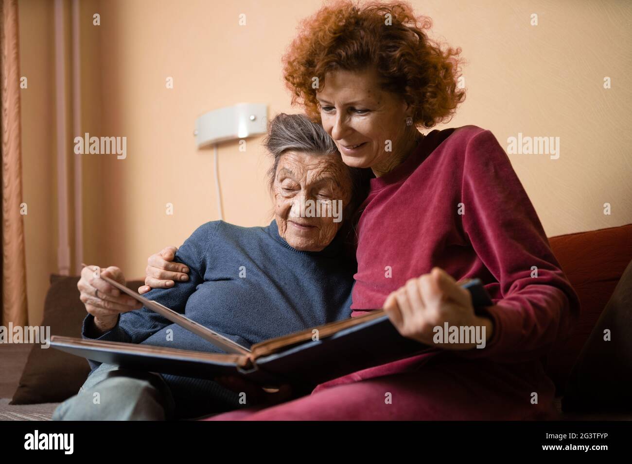 Senior woman and her adult daughter looking at photo album together on ...