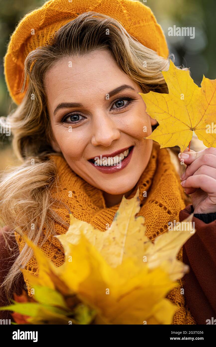 Close up. Young woman in beige knitted beret with autumn leaves in hand and fall yellow garden or park. Beautiful smiling young Stock Photo