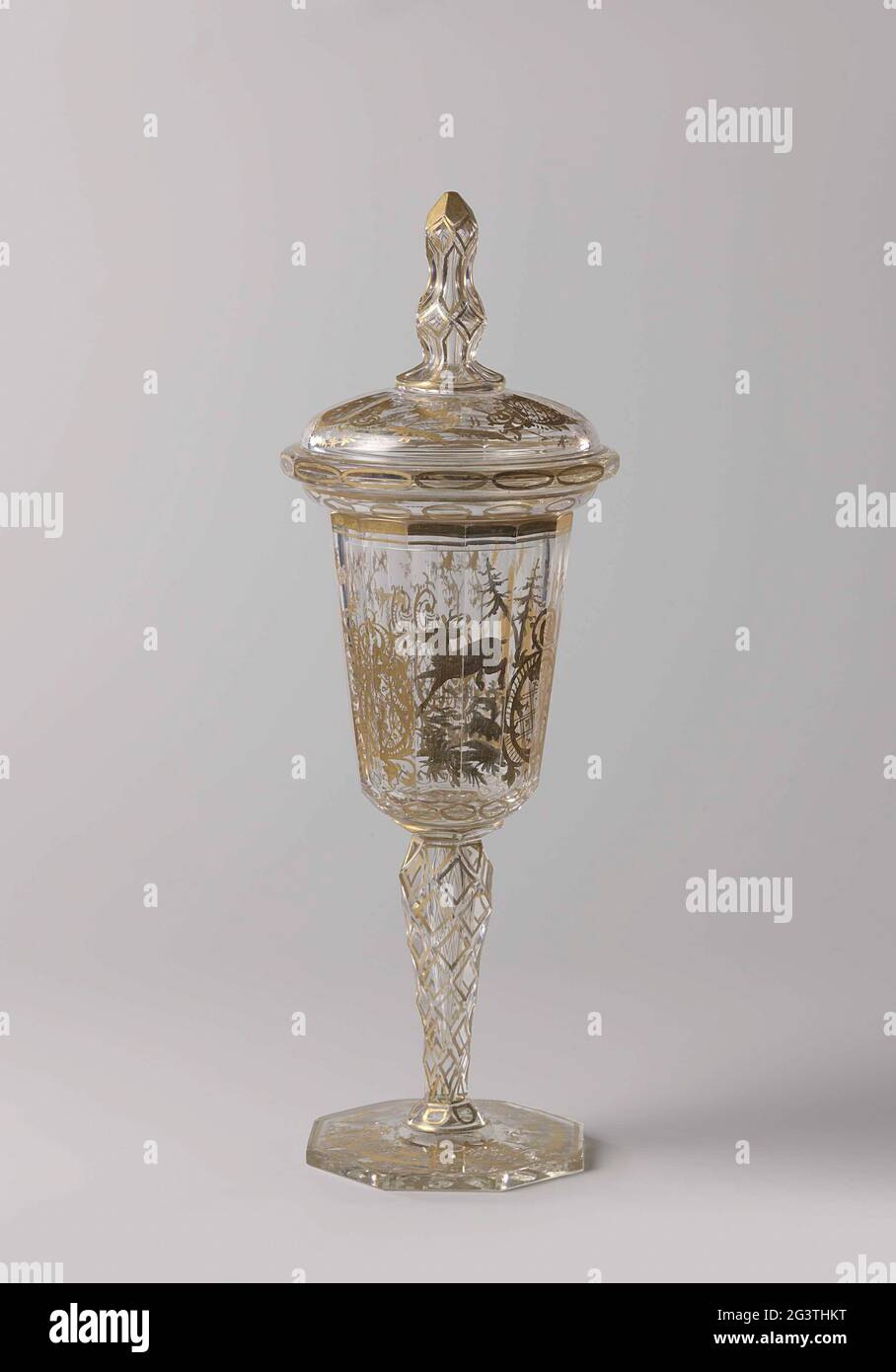 Cup with lid, with a yacht scene. Flat, octagonal, facet cut foot. Facet cut, baluster-shaped strain. Funnel-shaped, rounded and faceted chalice. Facet cut, vaulted lid with overrunning edge and a facet cut, baluster-shaped button, ending in a point. On the chalice in gold a yacht scene with a hunter with a gun. At the foot and the lid a deer, a stork and a dog between Rocaille ornament. The facets on foot, trunk and knob dipped off with gold. Stock Photo