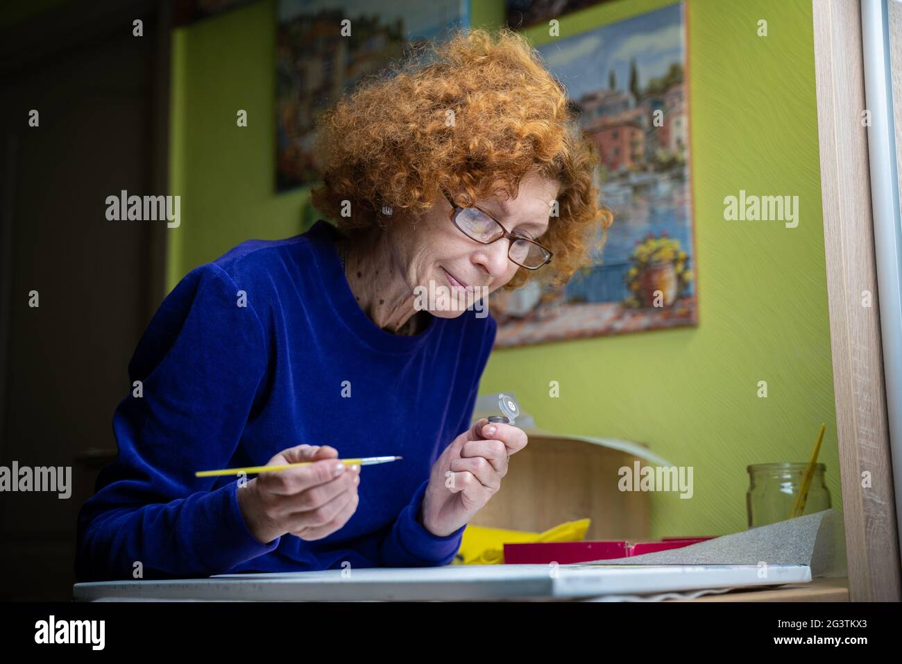 Learning new hobbies during the Coronavirus quarantine and lockdown. Senior woman artist paints at home. Attractive old woman dr Stock Photo
