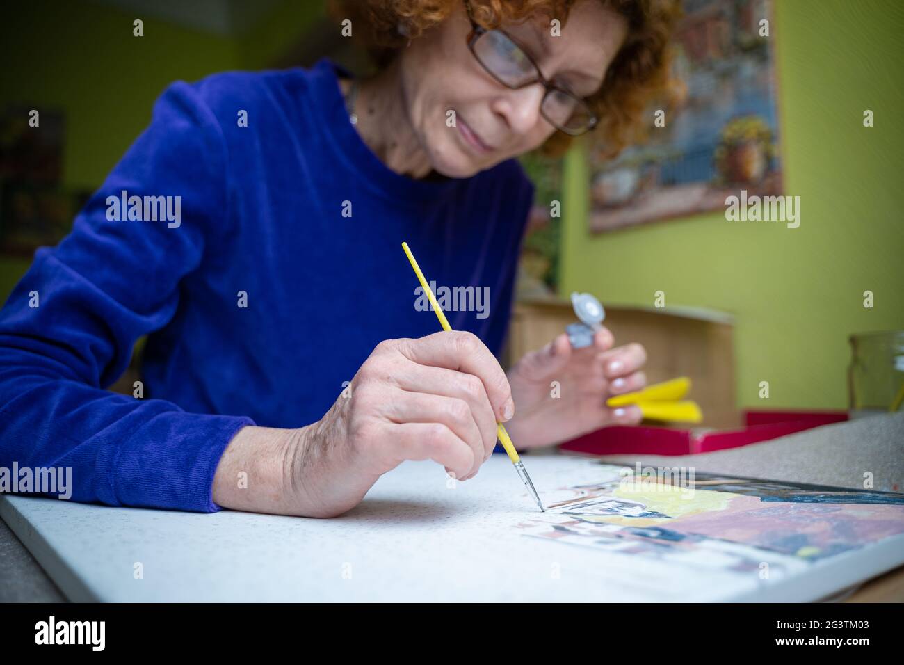 Happy elderly woman painting for fun at home. Senior Caucasian senior woman painting. Retirement hobby. Elderly woman painting o Stock Photo