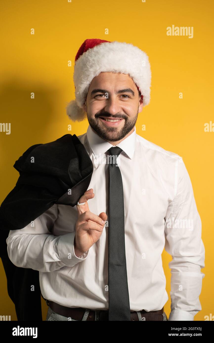 Bearded smiling handsome business man in Santa hat wearing grey suite posing holding his jacket on his shoulder hanging it behin Stock Photo