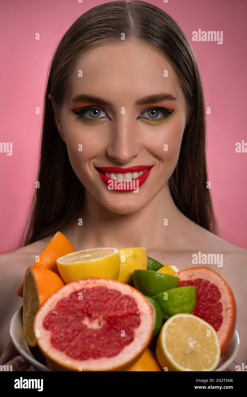 Beauty fashion model girl with beautiful make up, red lips, long healthy hair and bawl of colorful fresh cut citrus fruits in he Stock Photo