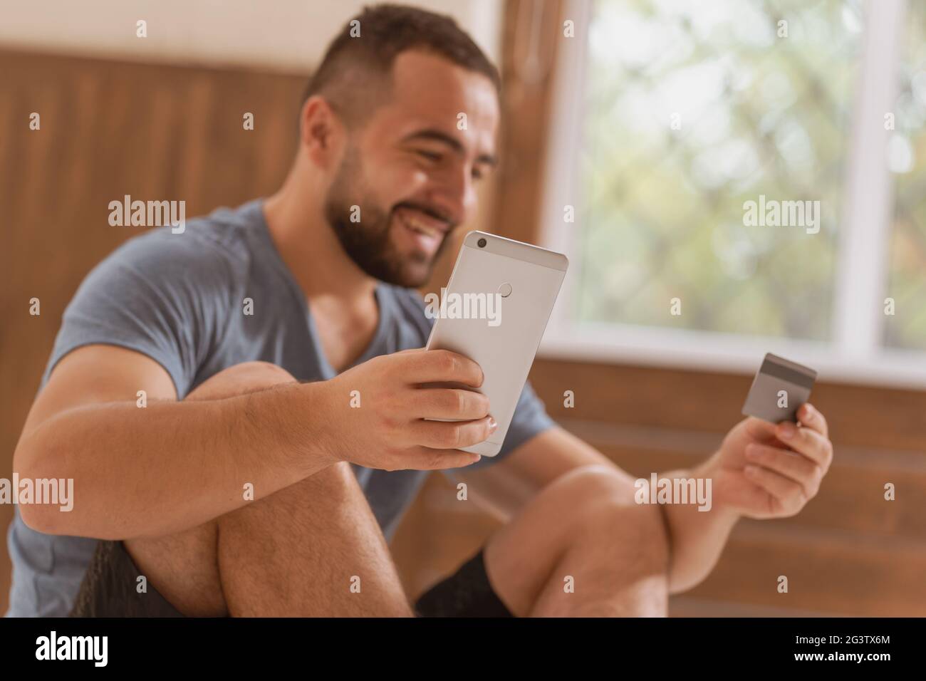 Low side shot of a cheerful man with smartphone and debit or credit card buying online equipment or doing sport bets and gamblin Stock Photo
