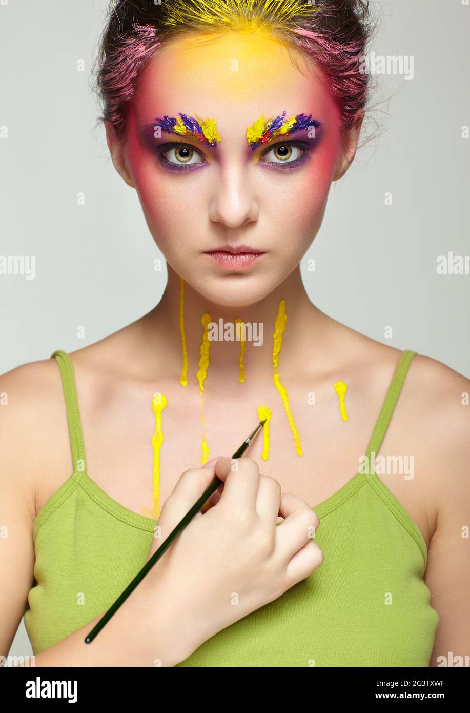 Female portrait with unusual face and body art make-up. Woman paints herself with a brush. Stock Photo
