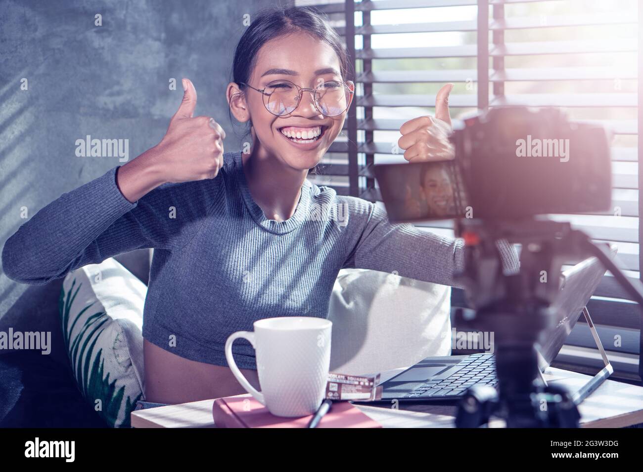 Young smiling woman vlogger showing thumbs up while recording her daily video blog Stock Photo