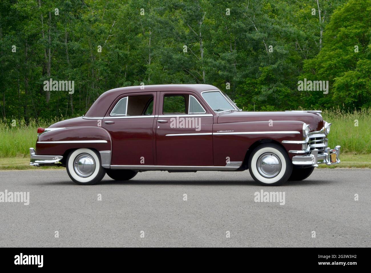 A side view of a 1949 Chrysler Windsor four-door sedan before a wooded background in soft light. Stock Photo