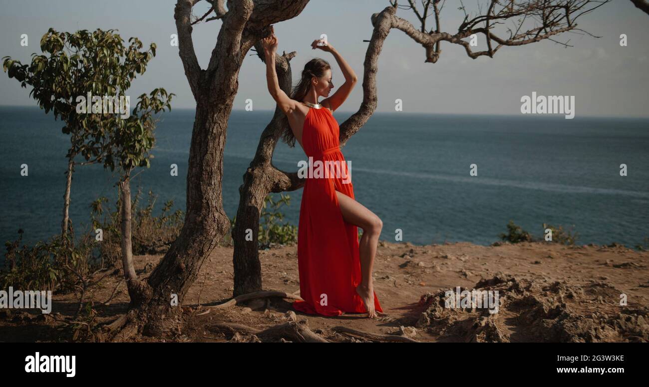 Beautiful woman in red dress on the sea shore cliff during over sea and ...