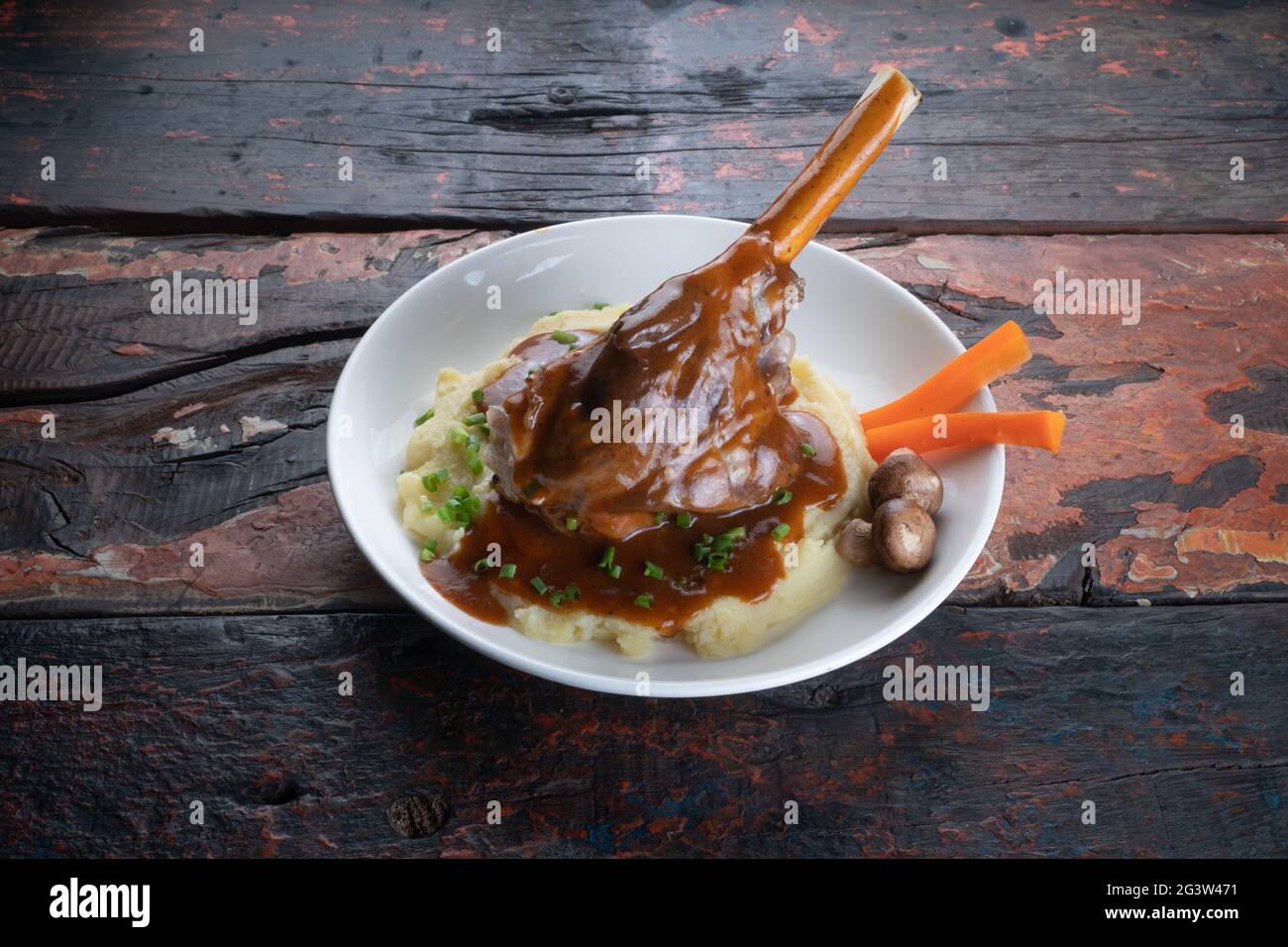 Turkish lamb shank in dark sauce with potato puree and vegetables on rustic wooden table Stock Photo
