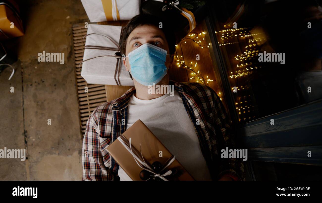 Depressed man in medical mask at home Christmas alone. Coronavirus on Christmas eve. New year holidays without friends and famil Stock Photo