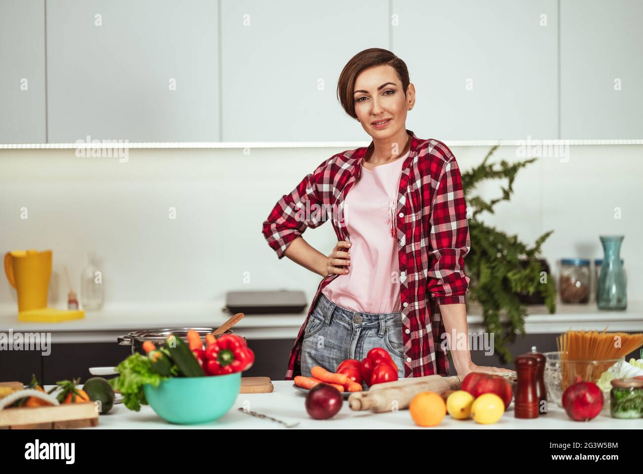 Pretty housewife cutting ingredients on table cooking a lunch standing in the kitchen with one hand on a side. Healthy lifestyle Stock Photo