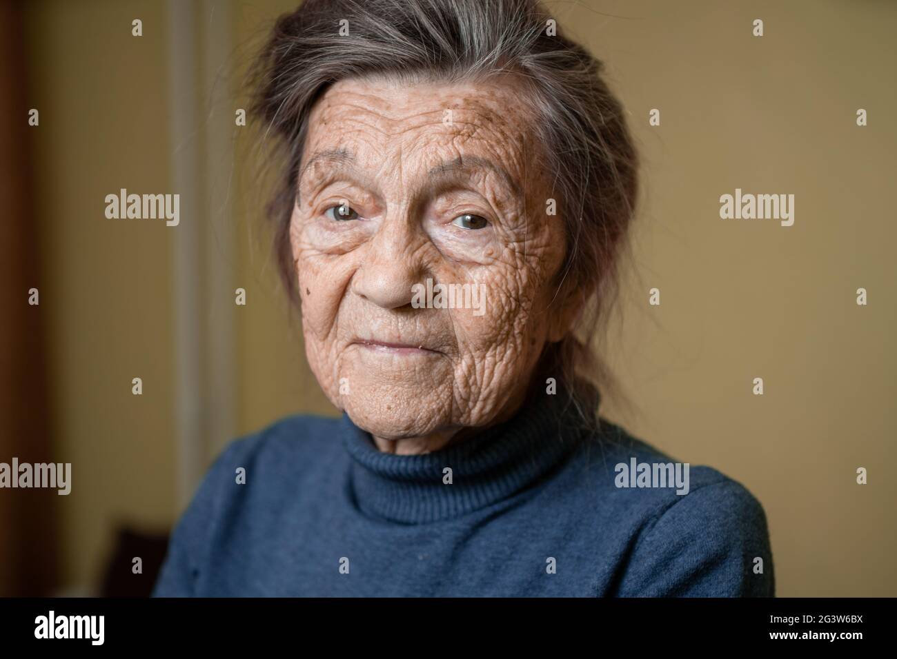 Older cute woman of ninety years old Caucasian with gray hair and wrinkled face looks at camera, cute kind look and smiles.Matur Stock Photo