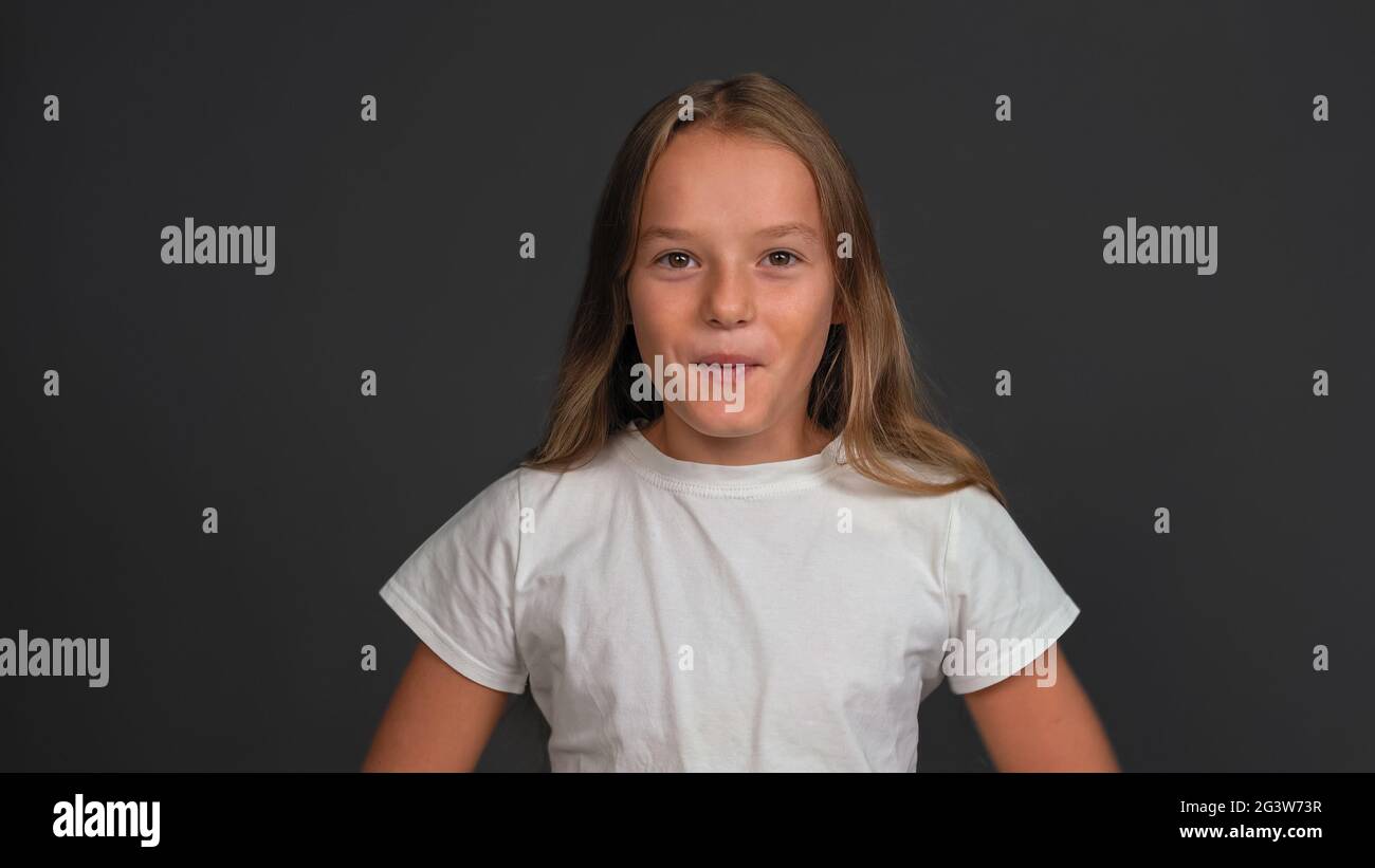 Amazed little girl standing looking happy surprised at the camera wearing white t-shirt isolated on dark grey or black backgroun Stock Photo