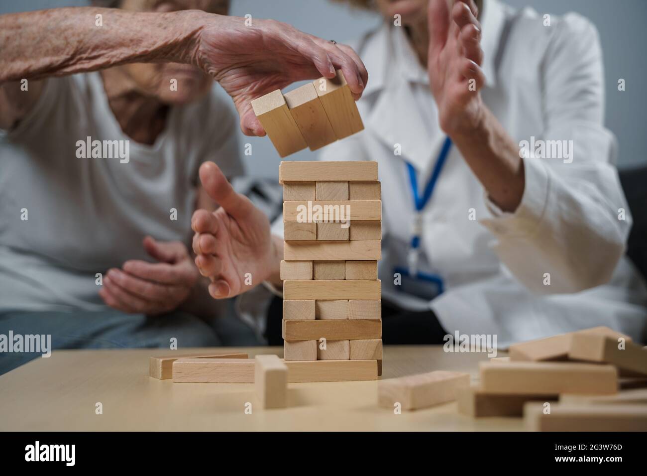 Senior woman practice skills, build wooden blocks, build tower and try not to let it fall, Jenga game. Old patient pull out bloc Stock Photo