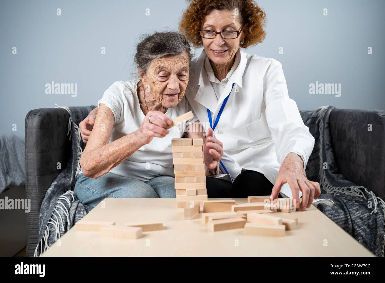 Senior woman practice skills, build wooden blocks, build tower and try not to let it fall, Jenga game. Old patient pull out bloc Stock Photo