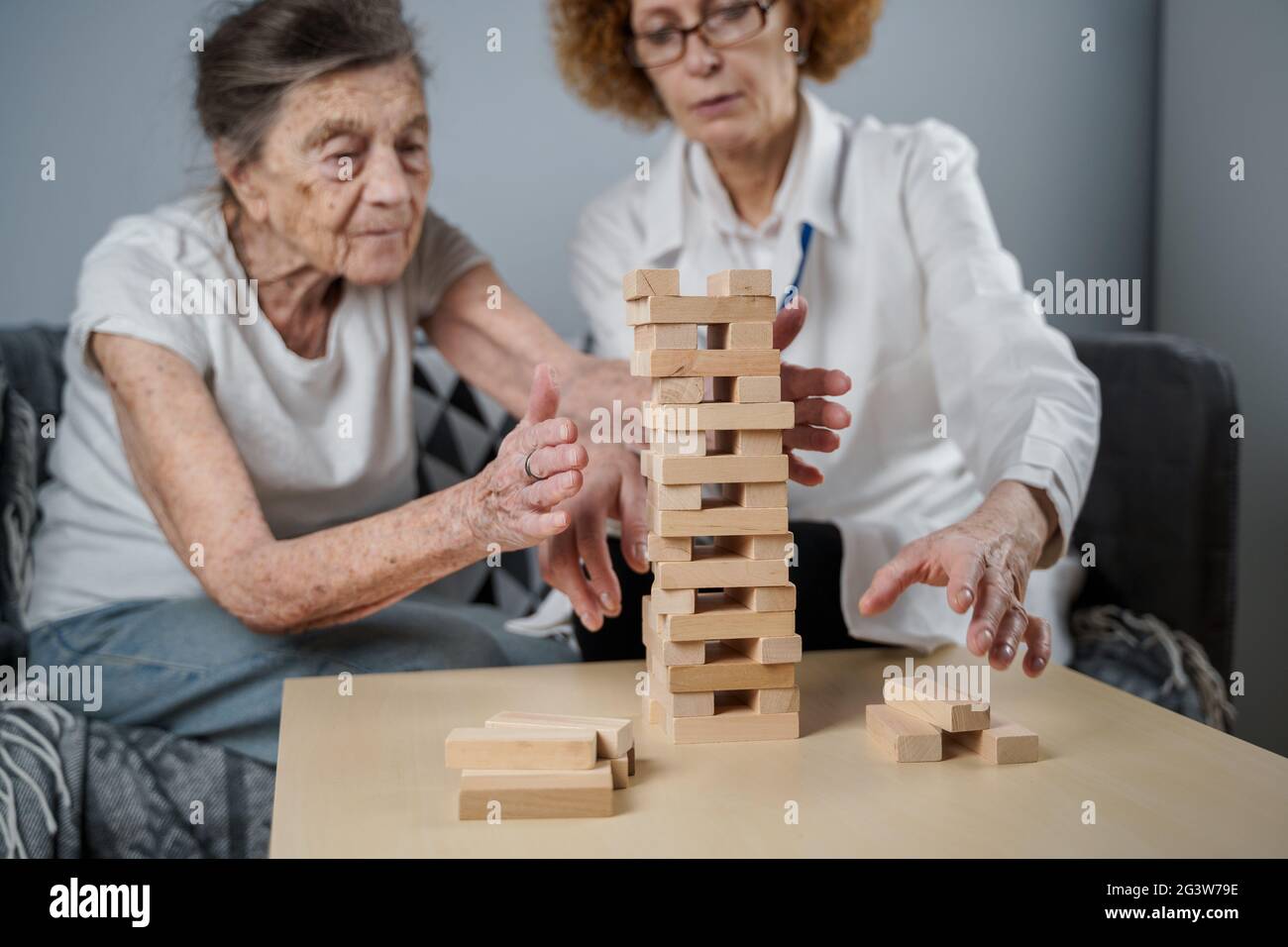 Dementia therapy in playful way, training fingers and fine motor skills, build wooden blocks into tower, playing Jenga. Senior w Stock Photo