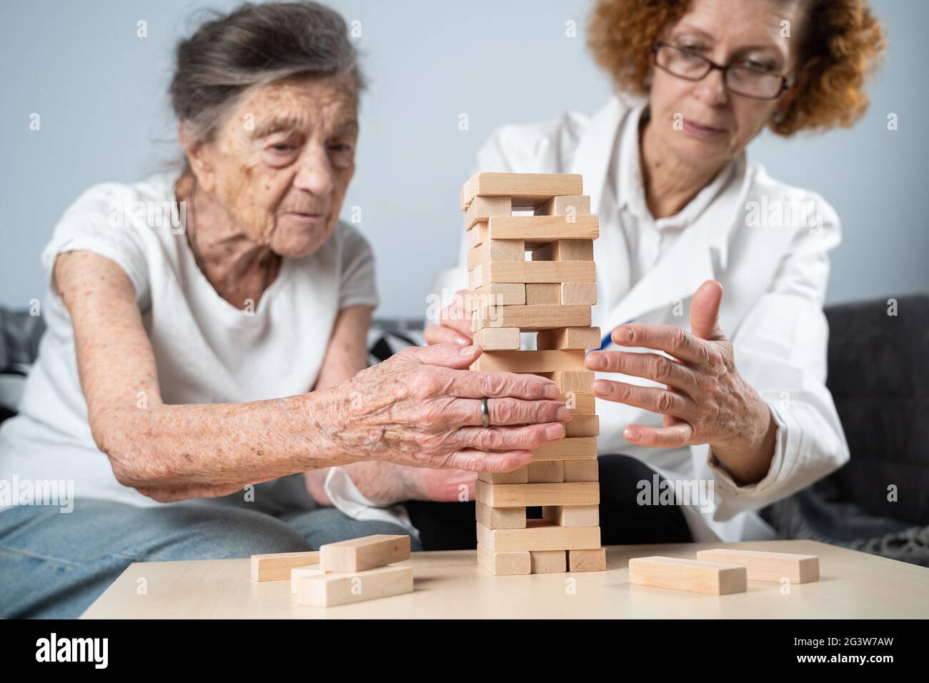 Senior woman playing Jenga, build tower of blocks. Elderly doctor in white lab coat, supporting senior patient, developing logic Stock Photo