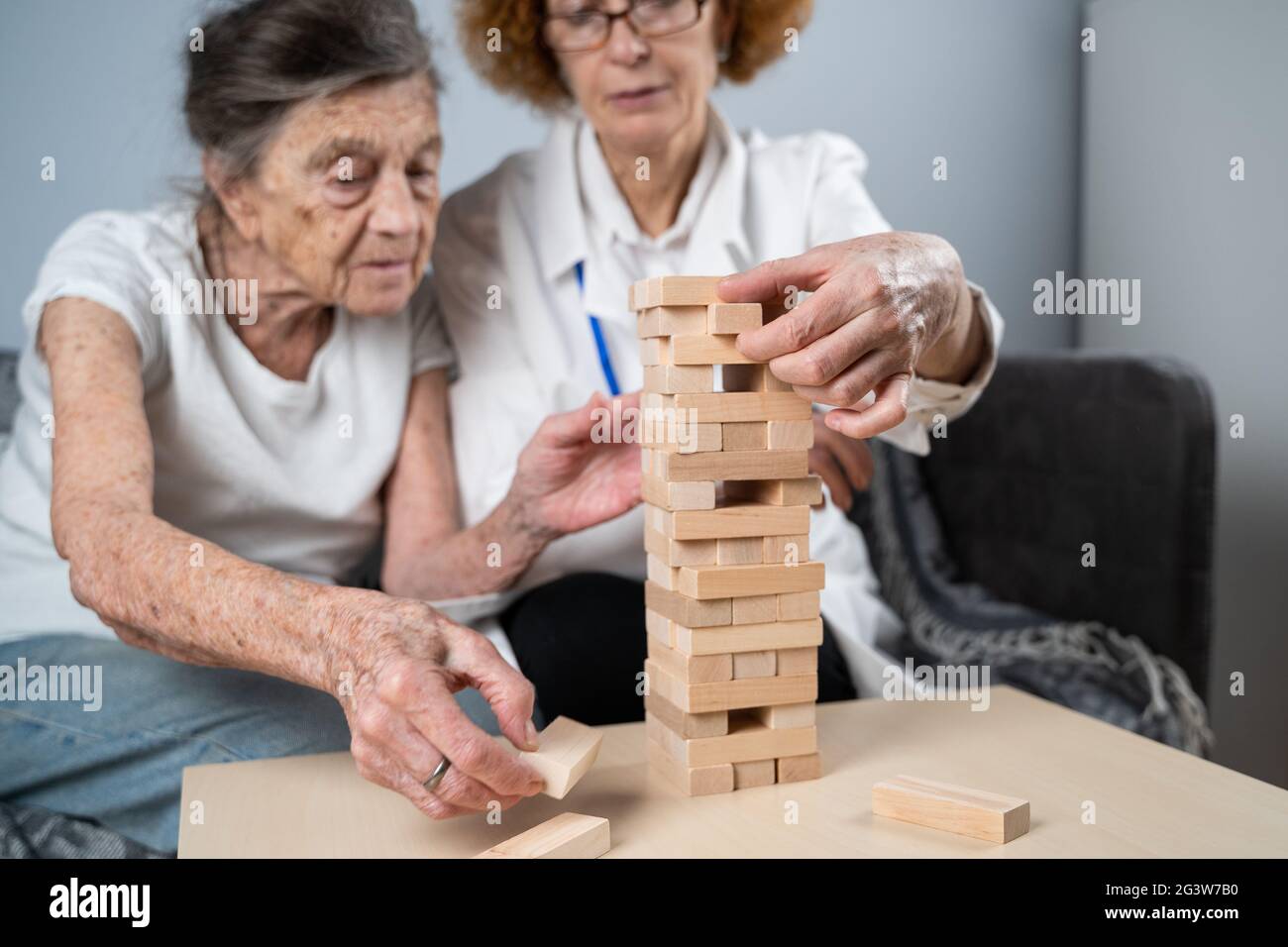 Senior woman playing Jenga, build tower of blocks. Elderly doctor in white lab coat, supporting senior patient, developing logic Stock Photo