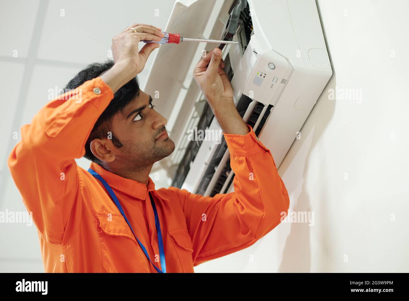Concentrated young Indian engineer in orange wear using screwdriver ...